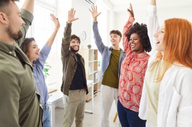 Ofisteki çok uluslu iş adamları bir toplantı sırasında el kaldırarak başarıyı kutluyorlar. Grup, ortak başarıları vurgulayarak, iş ortamında birlik ve takım çalışması gösteriyor.