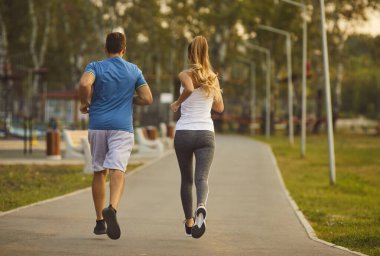 Sabahına enerji ver. Aktif genç spor çifti sabah birlikte şehir parkında koşuyorlar. Sıska kadın ve spor giysili bir adamın parkta koşu parkurunda birlikte koşuşunun arka görüntüsü..