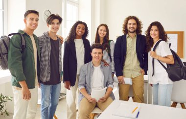 Bir grup genç üniversite sınıf arkadaşı ya da lise öğrencisi sınıfta arkadaş canlısı bir erkek öğretmenle birlikte kameraya neşeli bir şekilde bakıyorlar. Eğitim ve bilgi kavramı.