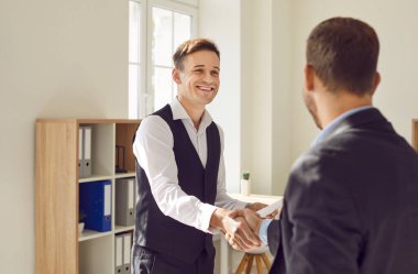 Mutlu işadamı ofisteki bir müşteri veya meslektaşına el sıkışarak başarılı bir anlaşma yaptı. Tokalaşma, takım çalışması ortaklığının gücünü ve varılan anlaşmayı simgeliyor..