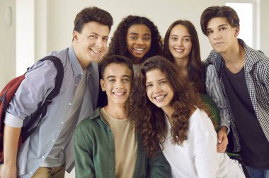 Bir grup mutlu, sırıtan lise öğrencisi yan yana durmuş koridordaki kameraya neşeli ve pozitif bakıyorlar. Kapalı alandaki kızların ve erkeklerin portresi.