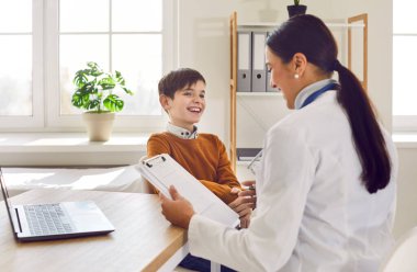 Gülümseyen kadın pediatrist muayenehanesinde mutlu bir çocuk hastayı muayene ediyor. Doktor, pratisyen hekim çocuk ile konuşuyor. Çocuk tıbbi bakım konsepti