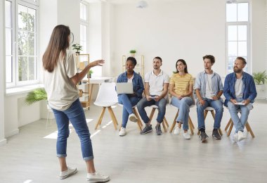 Kadın antrenör müşterilere danışmanlık yapıyor ya da öğretmenlik yapıyor. Kadın koç, hoparlör eğitimi, çeşitli insanlarla konuşmak, pazarlama atölyesindeki stratejiyi açıklamak.