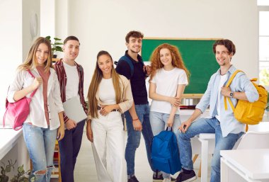 Bir grup okul, üniversite ya da üniversite öğrencisi, sınıf arkadaşları ve arkadaşlar sınıfta birlikte duruyorlar. Gündelik giysiler içinde birkaç mutlu genç sınıfta grup fotoğrafı çektirmek için poz veriyor.