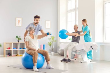 Sağlık çalışanları olgun insanların spor egzersizleri yapmalarına yardımcı oluyor. Kol ve spor salonunda topa uyum sağlıyorlar. Rehabilitasyon merkezinde emekli erkek ve kadına yardım eden fizyoterapist..