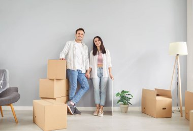 Yeni modern daireye taşındıktan sonra mutlu genç bir çift başarılı bir ipotek aldılar, karton paketlerin yanında durdular, istiflenmiş kutular, ev sahipleri, apartman sahipleri, taşınma kiracısı servisi