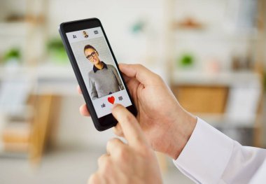 Yakın plan çekimde, dokunmatik ekranlı akıllı bir telefondaki internet gezici randevu uygulaması gibi bir profil için kalbi tıklatan bir kullanıcı görülüyor. Hızlı bir dokunuş, olumlu bir romantik ilginin işareti..