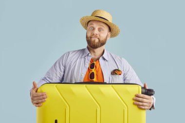 Gülümseyen ve mutlu bir adamın portresi, mavi arka planda bir bavul tutuyor. Tatile, tatil haftasonuna ya da yaz yolculuğuna hazır görünüyor..