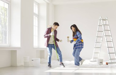 Gülümseyen genç çift yeni evlerinde duvarları boyarken dans edip gülüyorlar. Boyalı silindir tutan adam ve fırçalı kadın ev yenileme ve dekorasyon sürecinde eğleniyorlar..