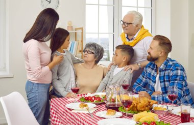 Büyük aile büyükannesini tebrik ediyor, oturma odasındaki aile yemeğinde ona sarılıyorlar. Ebeveynler, büyükanne ve büyükbabalar ve çocuklar birlikte konuşuyorlar. Aile tatilleri, aşk ve bakım konsepti.