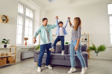 Mutlu gülümseyen aile, evdeki oturma odasında oğluyla eğleniyor. Bir çift havalanıyor. Pilot gözlüklü neşeli çocukları onunla uçak oyunu oynuyor..