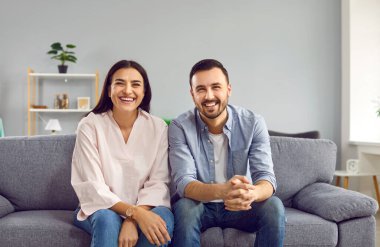 Evdeki kanepede mutlu ve mutlu bir ailenin portresi. Oturma odasındaki kanepede oturan neşeli genç adam ve kadın kameraya bakıyor ve gülümsüyor.