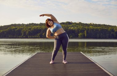Kilo vermek isteyen kasıtlı şişman kadın dışarıda spor eğitimi yapıyor. Spor kıyafetleri giymiş, göl kenarında spor antrenmanı yapan beyaz bir kadın..