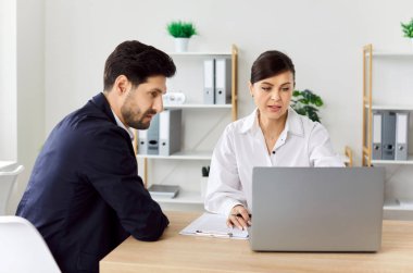 Ofiste gülümseyen iki şirket çalışanı. İş arkadaşları toplantı masasında oturmuş dizüstü bilgisayar ekranına bakıyor yeni projeleri veya girişimleri tartışıyor, şirketi analiz ediyorlar..