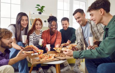 Mutlu, genç, etnik çeşitliliğe sahip insanlar öğrenciler ya da iş arkadaşları evde toplanıyor, kutulardan pizza dilimleri yiyor, konuşuyor ve birlikte gülüyorlar. Arkadaşlık ve parti konsepti.