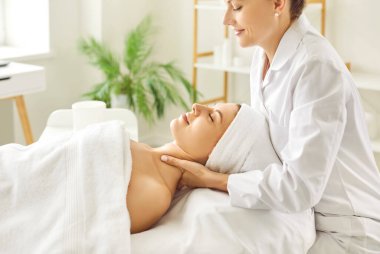 Kadın masör güzellik salonunda ya da kozmetoloji dolabında gözleri kapalı yatan genç bir kıza boyun rahatlatıcı masaj yapıyor. Profesyonel kozmetik uzmanı kaplıcadaki kadına masaj yapıyor..