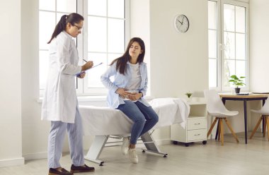 Karın ağrısı olan hamile bir kadın doğum kliniğindeki kadın doğum uzmanını ziyaret ediyor. Jinekolog, muayenehanedeki kanepede yatan kızı muayene ediyor ve randevu alıyor..