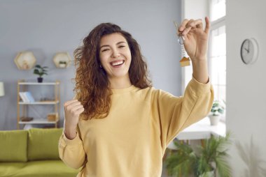 Evinde elinde anahtarlarla gülümseyen kıvırcık saçlı güzel bir kadının portresi. Emlak veya araba satın almayı önerirken el ele tutuşan mutlu yeni ev sahibi.