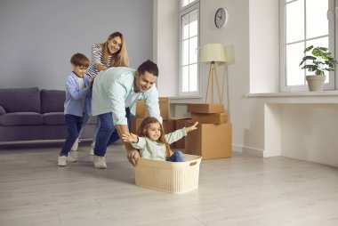 Genç, mutlu bir aile evdeki oturma odasında çocuklarla birlikte oyuncak sepetinde eğleniyor. Gülümseyen çift taşınma gününü yeni dairede kutluyor. Taşınma, emlak, ipotek konsepti.