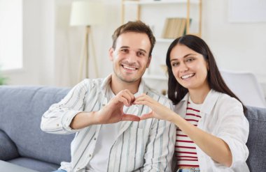 Mutlu ve gülümseyen bir çiftin portresi evde yapılan Sevgililer Günü kutlamasında elleri ile kalp şeklinde bir işaret oluşturuyor. Aşk, sevgi neşe ve tatilin romantik atmosferi..