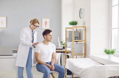 Kadın doktor ya da hemşire, hastane kontrolü sırasında akciğerlerini kontrol etmek ve nefes almak için steteskop kullanıyor. Bu sağlık ziyareti hasta sağlığı ve refahını güvence altına almaktadır..