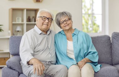 Yakın aşk ilişkisi, evlilik ve romantizm yaşayan sevimli evli bir çiftin portresi. Yakışıklı beyaz, olgun karı koca evdeki kanepede oturup kameraya bakarak gülümsüyor..