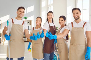 Mutlu temizlik ekibi elemanlarının toplu portresi, ev veya ofis temizliği sırasında gülümseyen ve onay veren. Temizlikçiler takım çalışması ve adanmışlık olumlu bir tutum sergiliyor..