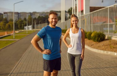 Gülümseyen çift şehir parkında fiziksel aktivite içinde. Erkek ve kadın, aktif bir spor yaşam tarzını benimserken, kentsel alanda çalışırken mutluluk saçıyorlar..