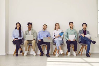 Bir iş seminerinde, şirket toplantısında ya da iş görüşmesinde çok ırklı bir grup insan. Beyaz bir ofis duvarının yanında dizüstü bilgisayarları ve panoları olan mutlu kadın ve erkeklerden oluşan bir takım.