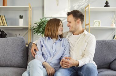 Oturma odasındaki kanepede oturan gülümseyen genç bir çiftin portresi. Birbirlerine sevgi ve şefkatle bakıyorlar. Sevgi dolu erkek ve kadın kucaklaşır, el ele tutuşur, duyguları ve duyguları paylaşır..