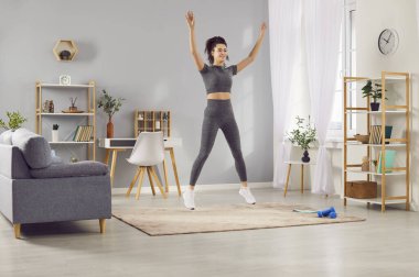 Sportif formda, spor kıyafetleriyle atlama egzersizi yapan genç ve güzel bir kadın, sabah egzersizi yapan bir kız, evde kadın antrenörü, fitness antrenmanı, kanepe sağlıklı aktif yaşam tarzı, vücut eğitimi. 