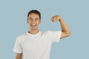 Gülümseyen genç bir çocuğun portresi zaferi el ele kutluyor. Stüdyonun mavi arka planında güç ve güç gösterisi yapıyor. Yakışıklı, neşeli adam, kazanan gibi gülümsüyor..