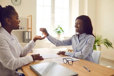 Mutlu, arkadaş canlısı, gülümseyen Afrikalı Amerikalı kadın emlakçı veya emlakçı ofiste müşteriyle buluşur, sözleşme imzalarlar ve ev sahibine anahtarlarını verir.