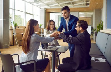 İş yerinde iş ekibi toplantısı. Modern ofis içinde dizüstü bilgisayarın etrafında toplanan bir grup mutlu insan el ele tutuşuyor. Takım çalışması, işbirliği, destek, anlaşma kavramı