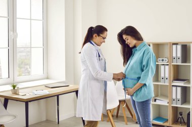 Doktor, genç hamile bir kadının karnını ölçer. Kadın doğum uzmanı geçen üç ay içinde hamile bir kızın karnına mezura bağlamış. Hamilelik, sağlık bakımı, tıbbi muayene konsepti.