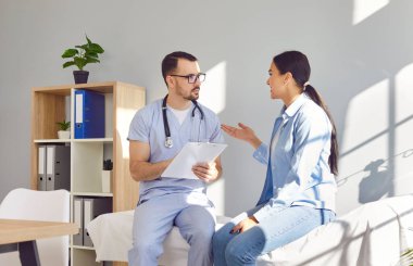 Erkek doktor, hastane muayenesi sırasında kadın bir hastaya uzman rehberlik ve tıbbi tavsiyelerde bulunur. Görüntü profesyonelliği ve uzmanlığı yansıtıyor..