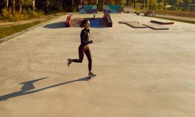 Şehir parkında koşan neşeli genç bir kadının en iyi manzarası. Esmer kız spor giyinmiş, dışarıda koşuyor. Kilo kaybı, sağlıklı yaşam tarzı, spor antrenmanı ve doğa konseptinde uygunluk..