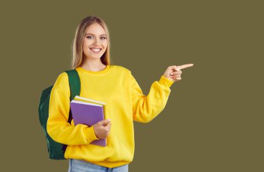 Sırt çantalı ve defterli mutlu öğrenci kız haki arka planda fotokopi alanını işaret ediyor. Sarı kazaklı ve kot pantolonlu sarışın kız. Reklam afişi, eğitim, iyi teklif konsepti.