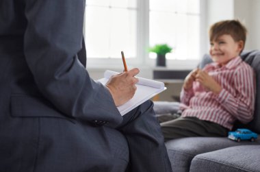 Çocuk hastasıyla konuşan profesyonel psikolog ya da psikoterapist. Elinde kalem ve not defteri olan bir kadın kanepede oturan ve kağıda notlar yazan bir çocukla konuşuyor. Çocuk terapisi konsepti
