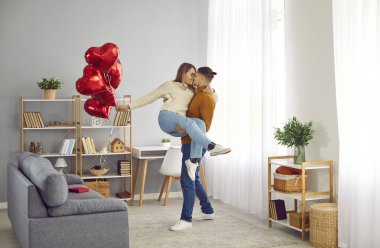 Genç esmer bir adamın kucağında bir kızı tutarken tam vücut fotoğrafı. Elinde kırmızı kalp şeklinde balonlar tutan kadın. Aşık genç bir çift. Dikkat, şefkat ve sevgililer günü konsepti.