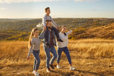 Mutlu gülümseyen genç bir aile. Oğlu ve kızı dışarıda yürüyor. Tarlada güzel doğanın tadını çıkarıyor. Anne, baba ve iki çocuk güneşli bir günde yürüyüş yapıyorlar. Aile eğlence konsepti.