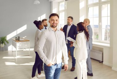 İş arkadaşları arka planda dururken kendine güvenen işadamı gülümsüyor. İş adamları ön planda erkek liderle konuşuyor. Arkasında ortakları olan olumlu bir adam kameraya bakıyor.