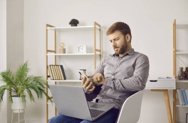 İş adamı cep telefonu ve dizüstü bilgisayar kullanıyor. Evdeki dizüstü bilgisayarlı sandalyede oturan genç adam, cep telefonunu tutuyor, sosyal medya uygulamasından haber okuyor, telefon numarasını çeviriyor ya da mesaj yazıyor.