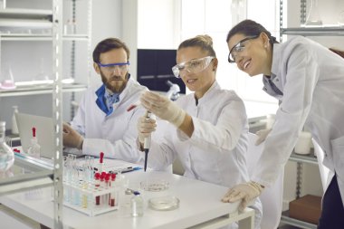 Science laboratory workflow. Group of scientist researcher happily smiling discussing new vaccine or innovative drug getting good experiment result looking at glass test tube with sample.