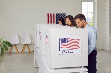 Group of USA citizens casts votes in booths during election day in a vote center office setting. The American flag proudly placed on booth, symbolizing the essence of civic duty and national pride.