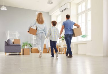 Backside view of an parents and son celebrate relocation to a new home, holding moving boxes in a display of family togetherness. New property ownership, real estate, and shared wealth.