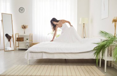 Good morning cleaning, starting new day, woman makes her bed, putting sheet to smooth wrinkles, flat sheet, blankets, duvet, cushions in modern bedroom interior design, comfortable stylish apartment 