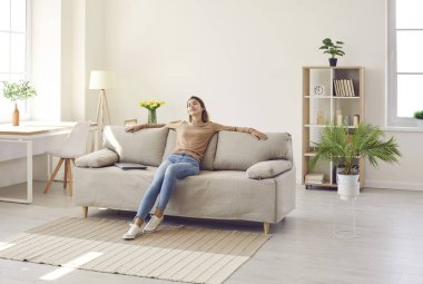 Clam millennial Caucasian girl sit rest on sofa in living room sleep or take nap. Happy young woman relax on comfortable couch furniture at home, daydream doze, relieve negative emotion. Stress free.