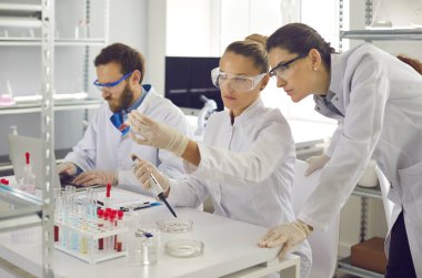 Group of scientist working in laboratory. Woman researcher analyzing chemical liquids take samples with pipette. Female assistant looking at experiment result in test tube. Science and research