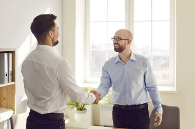 Two happy smiling men shaking hands standing in office finishing meeting, celebrating success, business achievement, making a good deal, , signing a contract or greeting new employee.